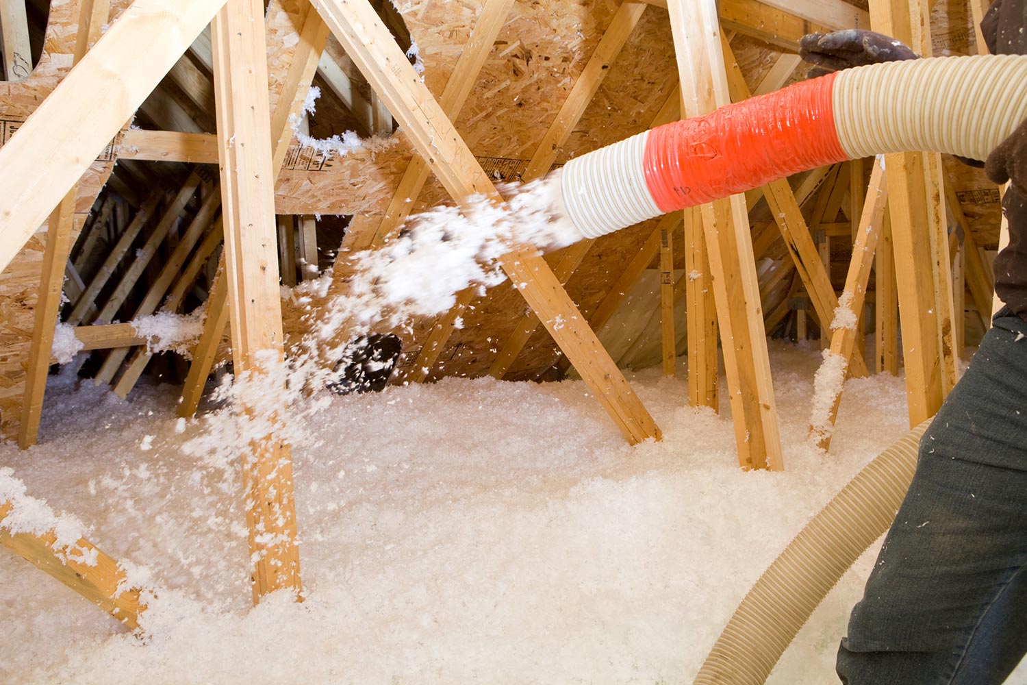 vWorker spraying blown fiberglass insulation between attic trusses
