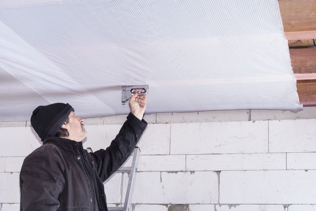 builder attaches vapor barrier to wooden beams on the ceiling