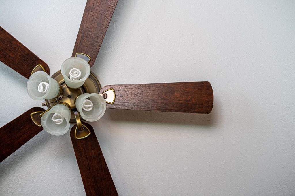 A ceiling fan with wooden blades and bulbs
