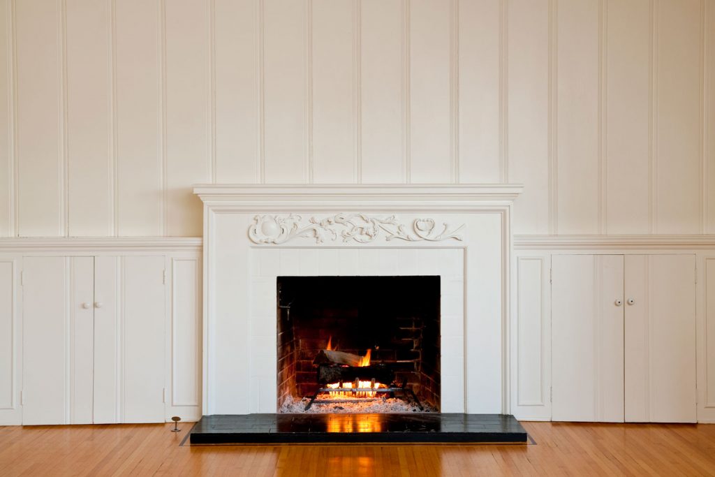A fireplace with white mantel and white panel walls