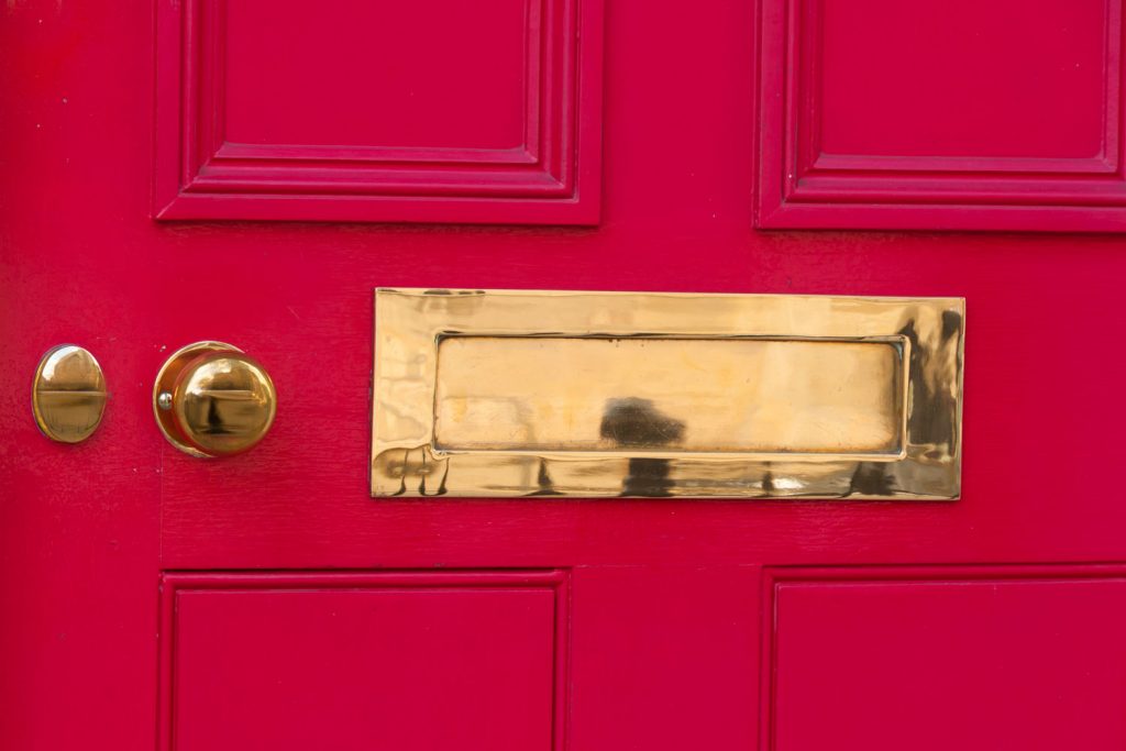 A gold plated mail slow and door knob on the red door