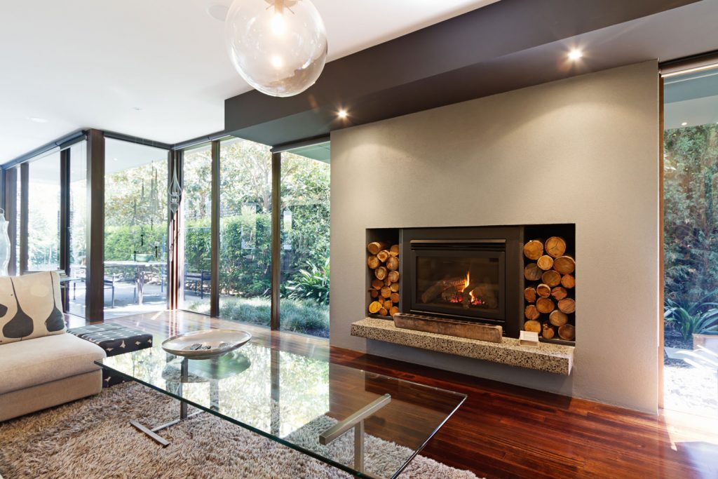 A gorgeous modern fireplace with logs on the side of an architectural designed wall for a gas fireplace