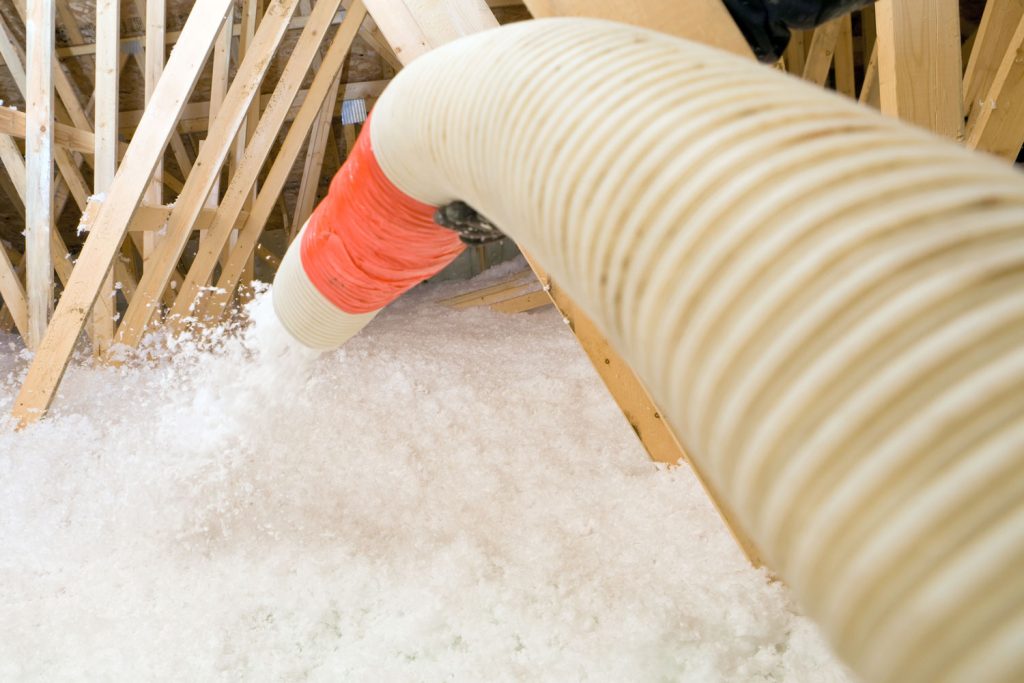 A hose spraying blow-in insulation to the attic flooring