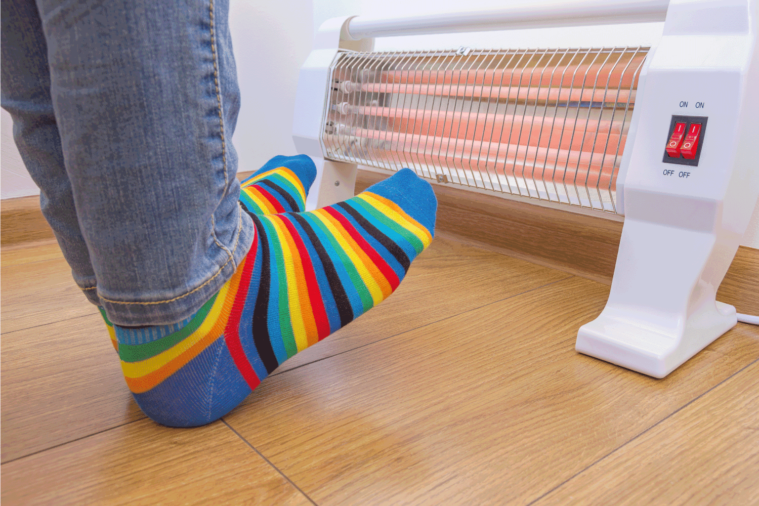 A person wearing bright rainbow-colored socks and warms cold feet near an electric heater. Infrared halogen heater at home