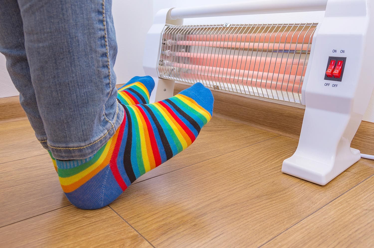 A person wearing bright rainbow-colored socks and warms cold feet near an electric heater
