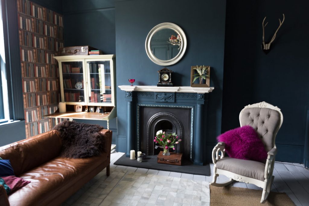 A vintage style living room with a small library, dark blue painted walls and a fireplace matching the trims