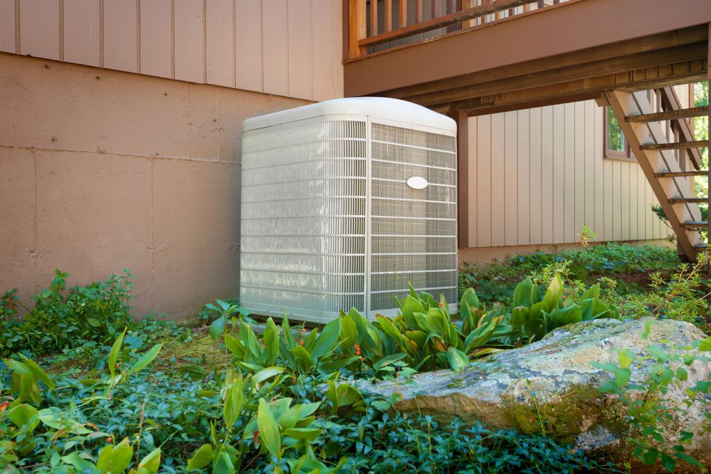 A white cased heat pump on the side of the house