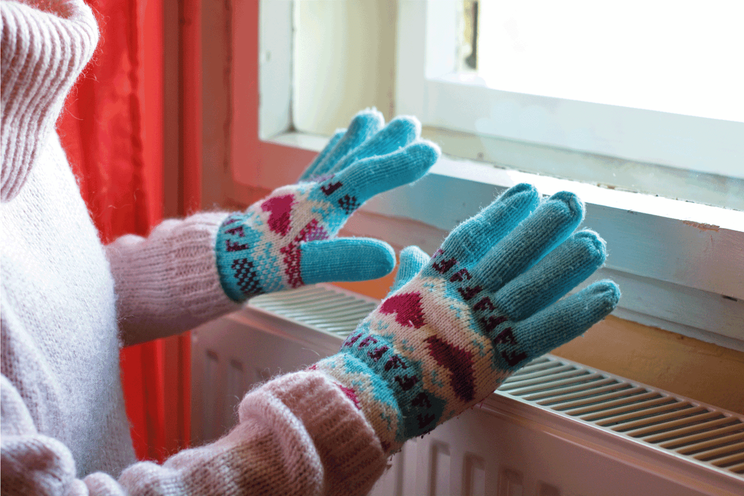 A woman hands in wool gloves warms near the heater