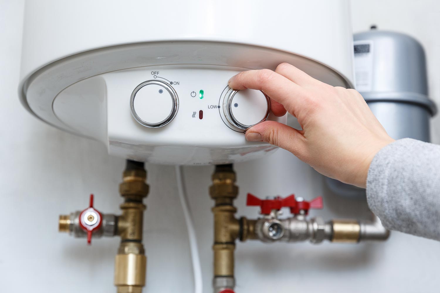 Female hand puts thermostat of electric water heater (boiler) in low low power consumption mode