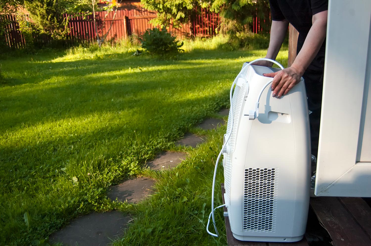 Female hands moving a portable air conditioner into a house