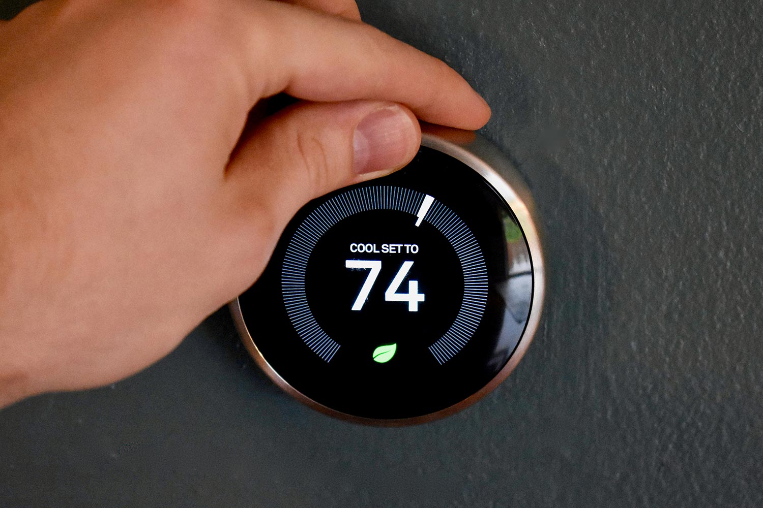 Hand adjusting temperature on smart thermostat to save energy and money