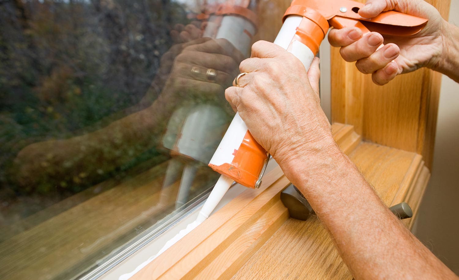 Hands applying weather seal caulk to window frame
