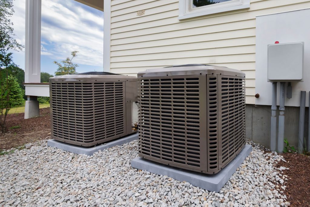 Heat pump units placed on a concrete pedestal surrounded with white stone to avoid getting dirty