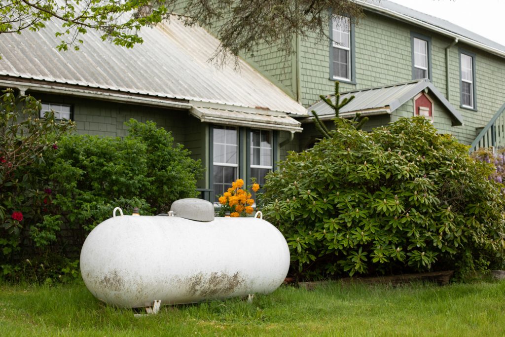 Large propane tank in the yard of a rural home, with a house in the background and space for text on the right