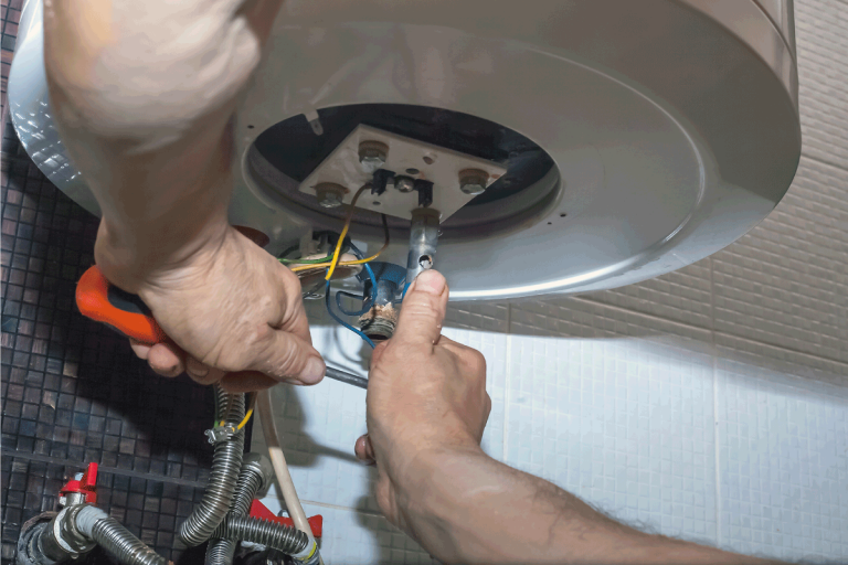 Plumber man repairing electric boiler in bathroom. Repairman hand are fixing broken water heater. Rheem Water Heater Leaking—What To Do