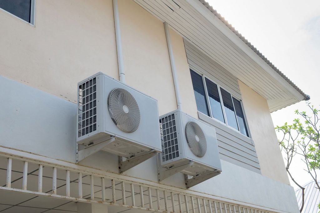 Two air conditioning condenser units mounted outside a two story house