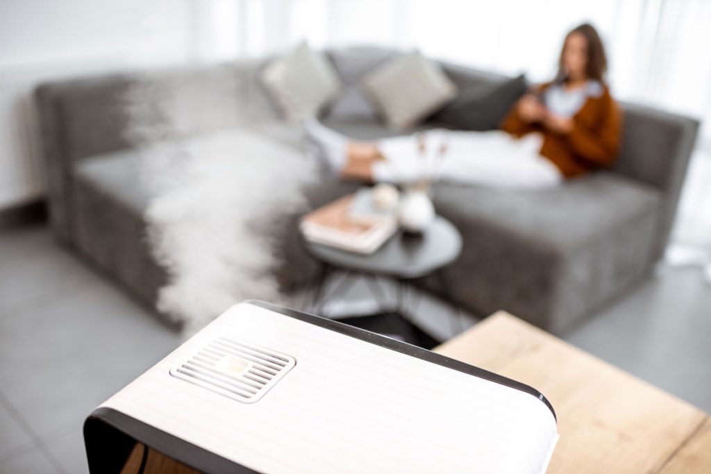 Woman relaxing on the couch at home with working air humidifier on the foreground.