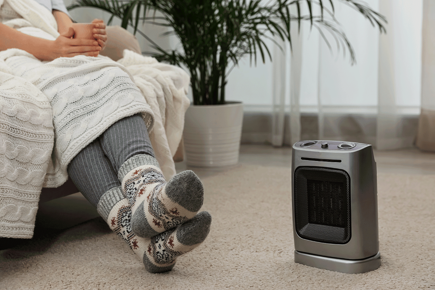 Woman warming legs near halogen heater at home