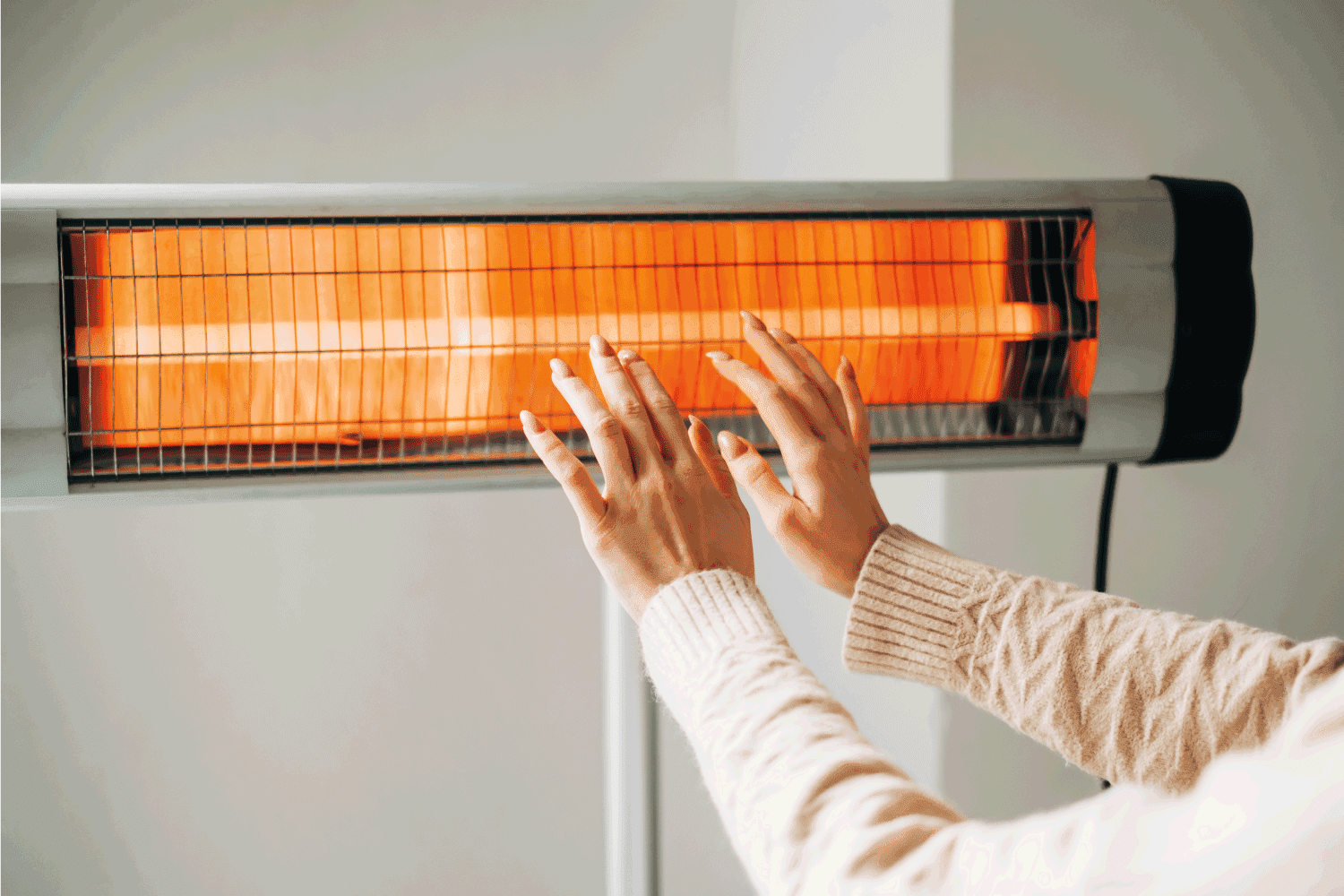 Woman warms up hands over electric heater. Concept of the need for good central heating