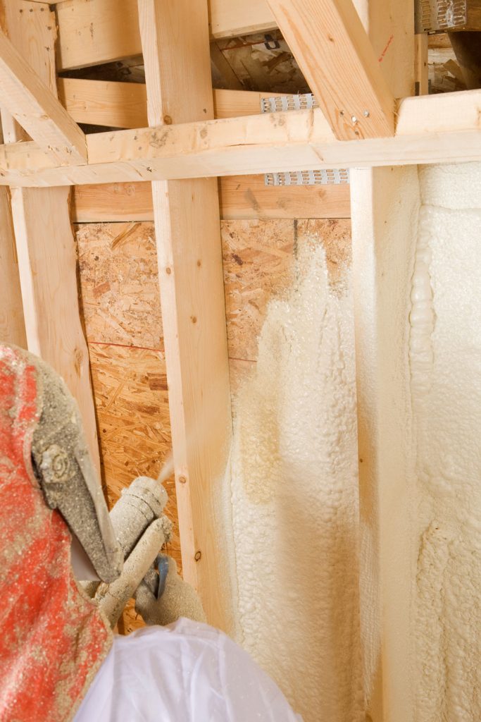 Worker applying foam insulation on the wall framing