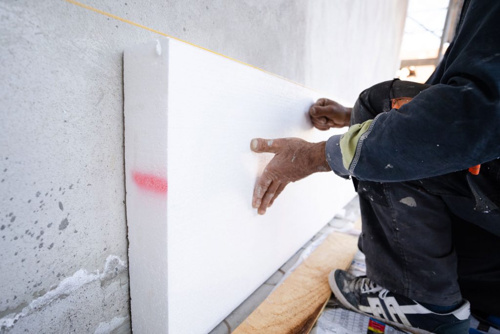 Worker placing styrofoam sheet insulation to the wall at construction site
