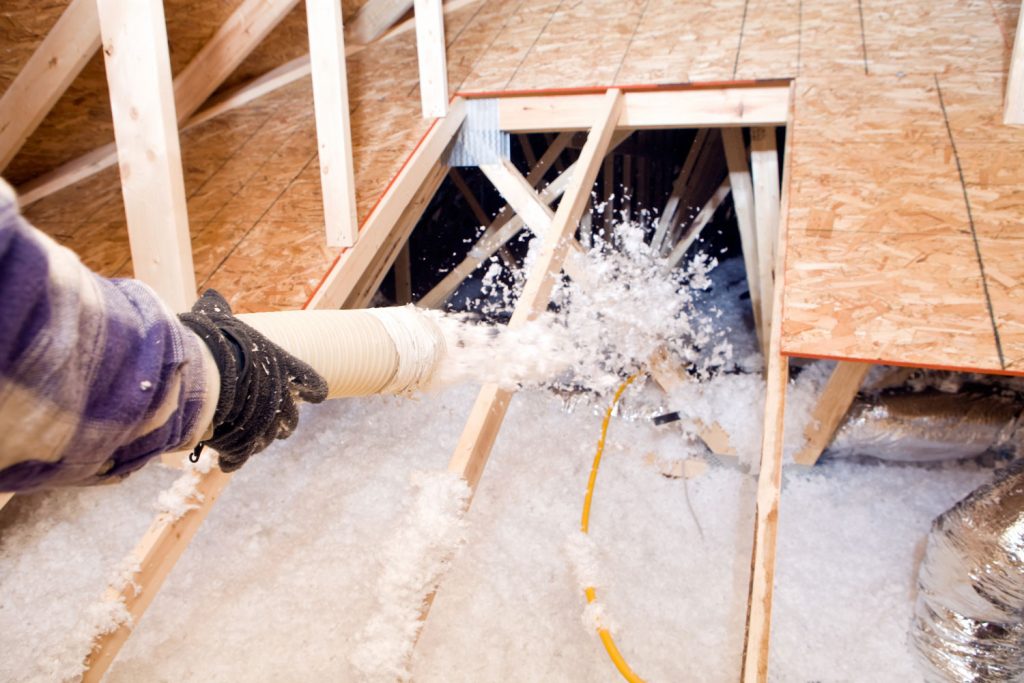 Worker spraying blow-in insulation to the attic floor joist