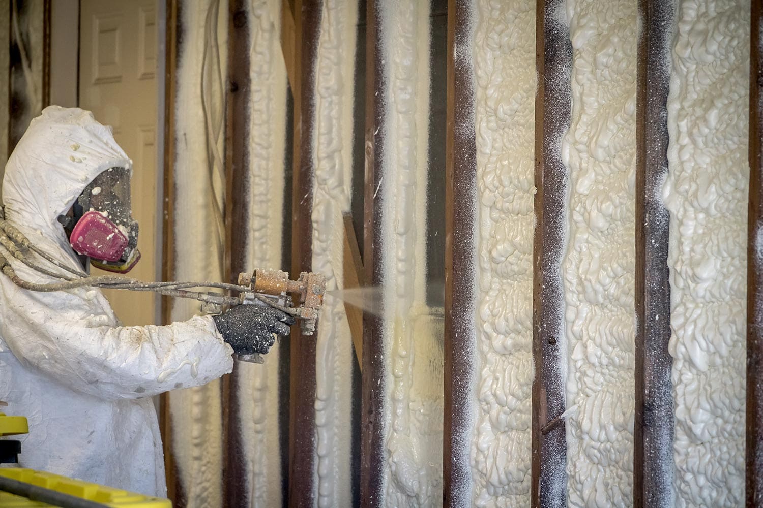 Worker spraying closed cell spray foam insulation on a home