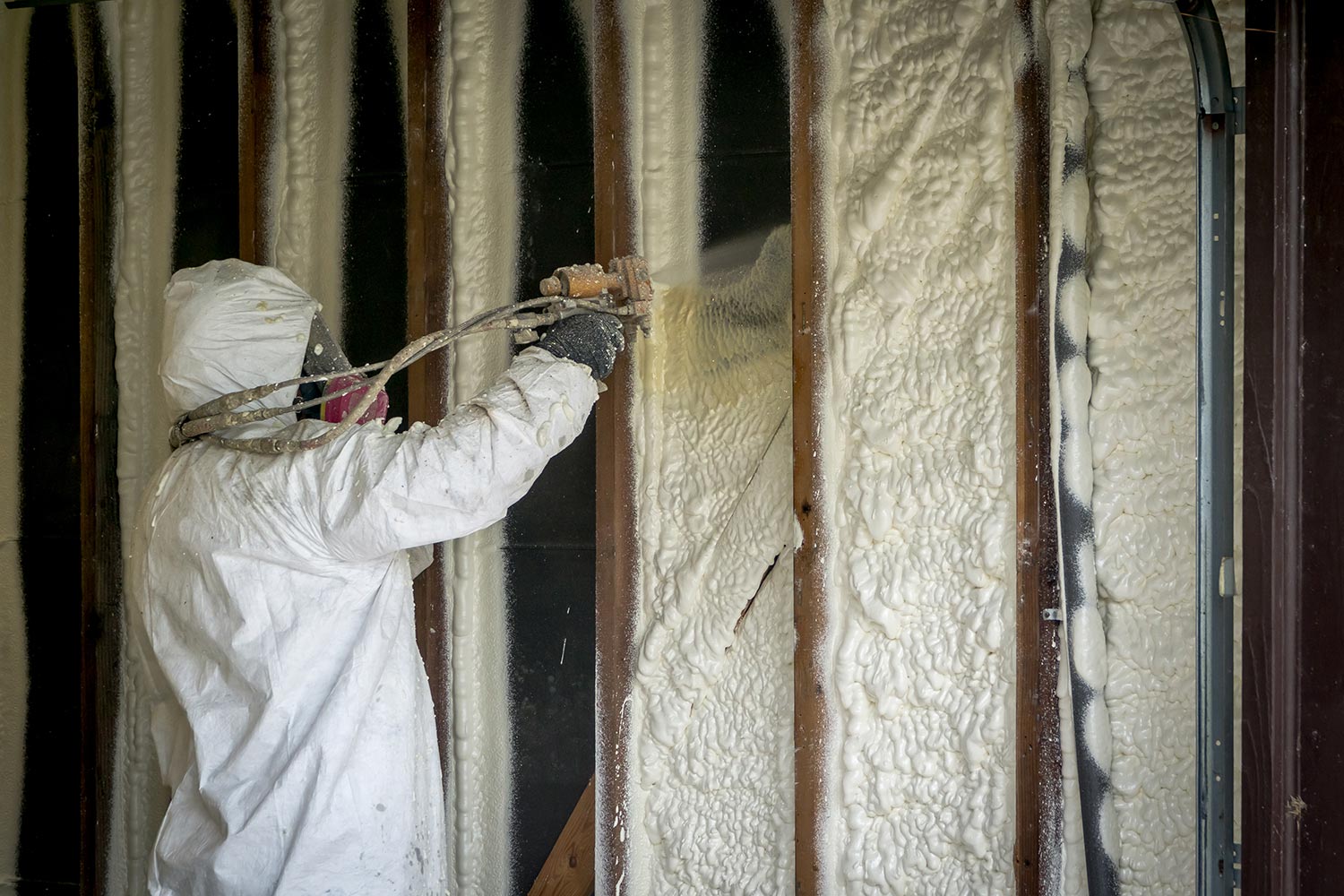 Worker spraying closed cell spray foam insulation on a home