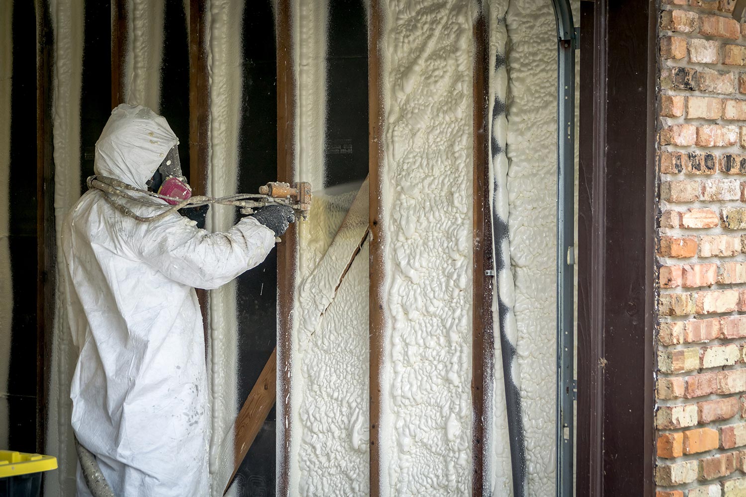 Worker spraying open cell spray foam on the wall of a home
