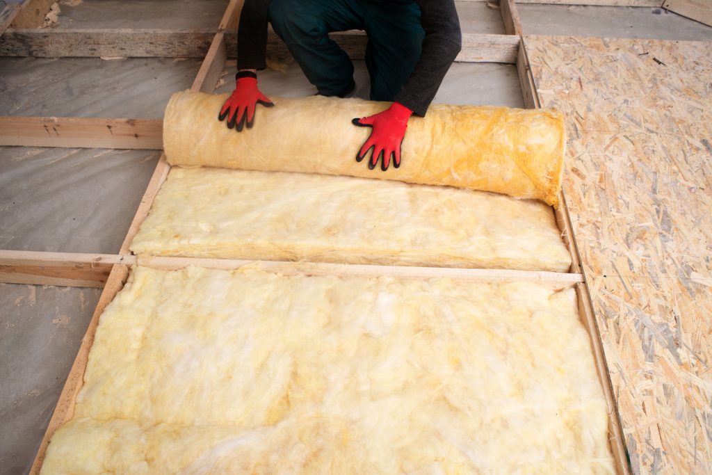 Worker unrolling a block of fiberglass insulation, How To Insulate A Sunroom (Inc. The Ceiling)