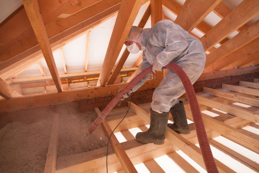 Worker with a hose is spraying ecowool insulation in the attic of a house