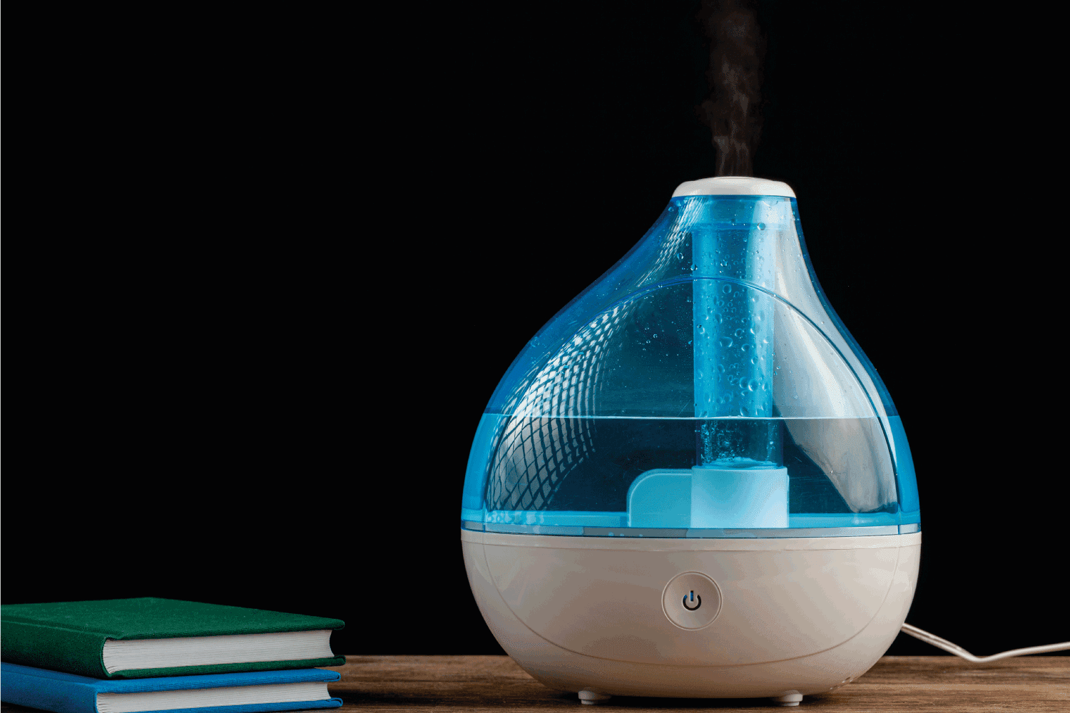 ultrasonic air humidifier creating cool mist water vapor. Stack of books are also seen on wooden tabletop.