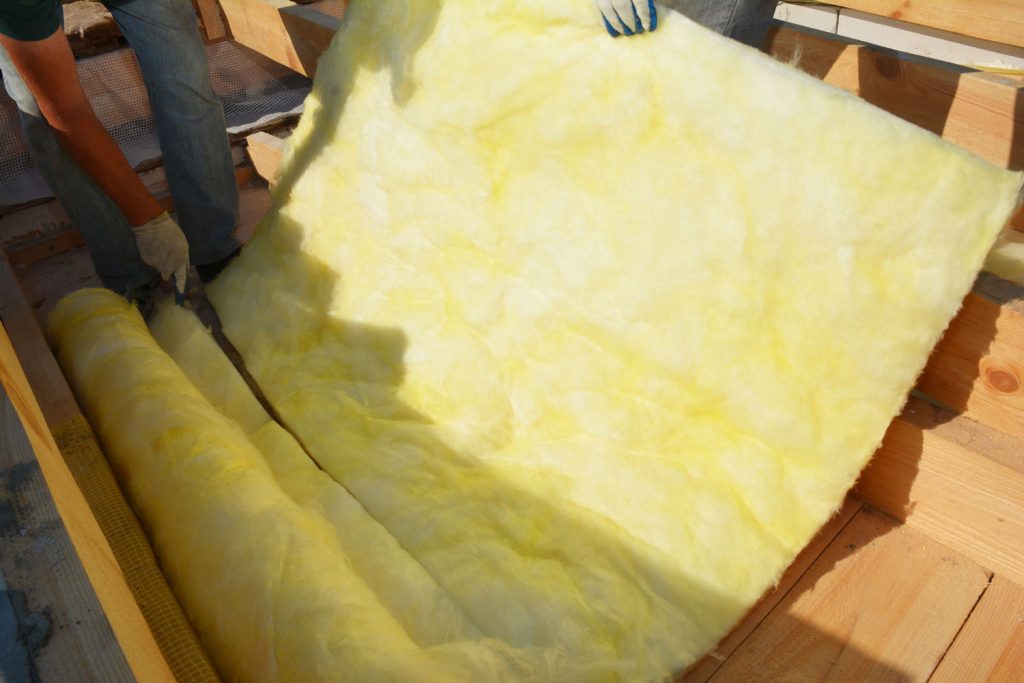 A building contractor is unrolling glass wool batt or blanket, and is cutting a sheet for the roof insulation.