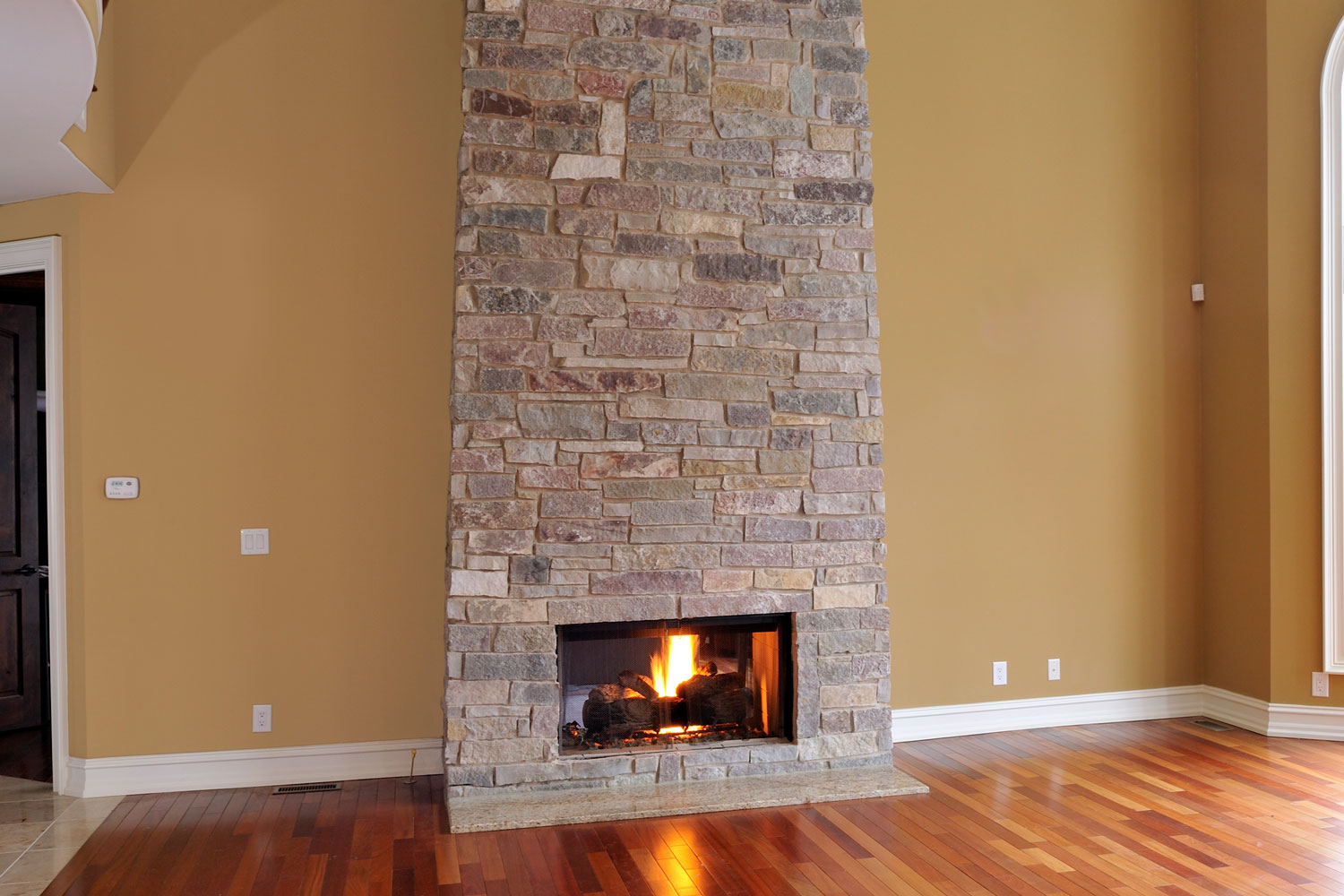 A gorgeous stone cladding fireplace in the living room with wooden flooring and tan walls