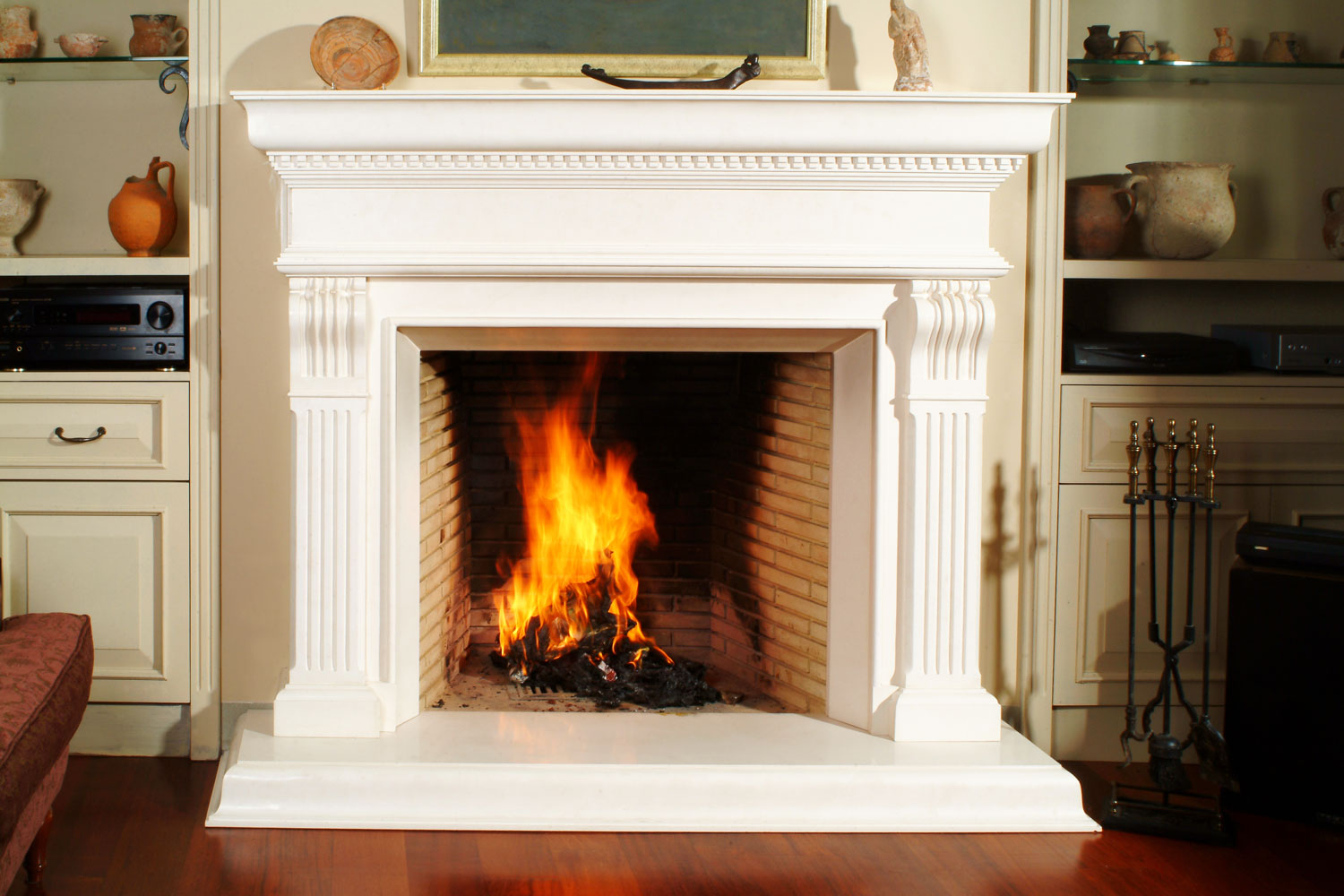A gorgeous white fireplace mantel with wood burning in it