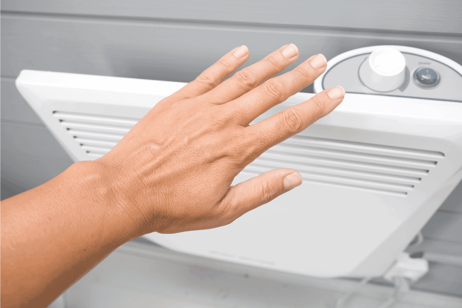 A hand checking temperature of heating convector on the wall, air heating the house in fall and winter