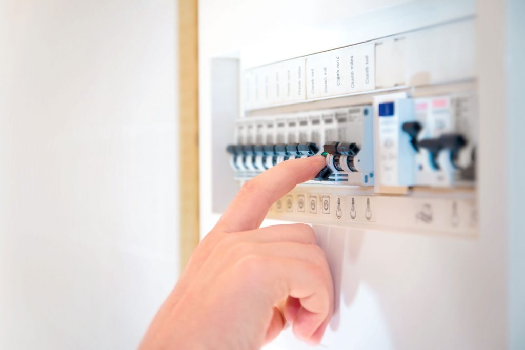 A human hand is cutting out, turning OFF a circuit breaker fuse box switch.