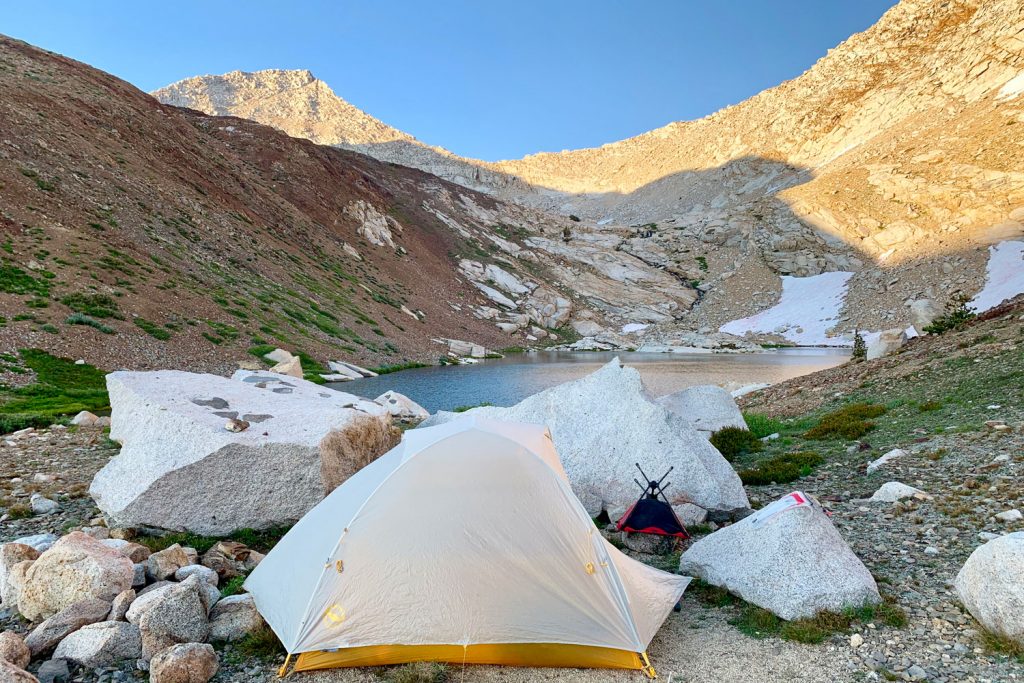 A tent setup near a small body of water for a scenic view of the mountain range