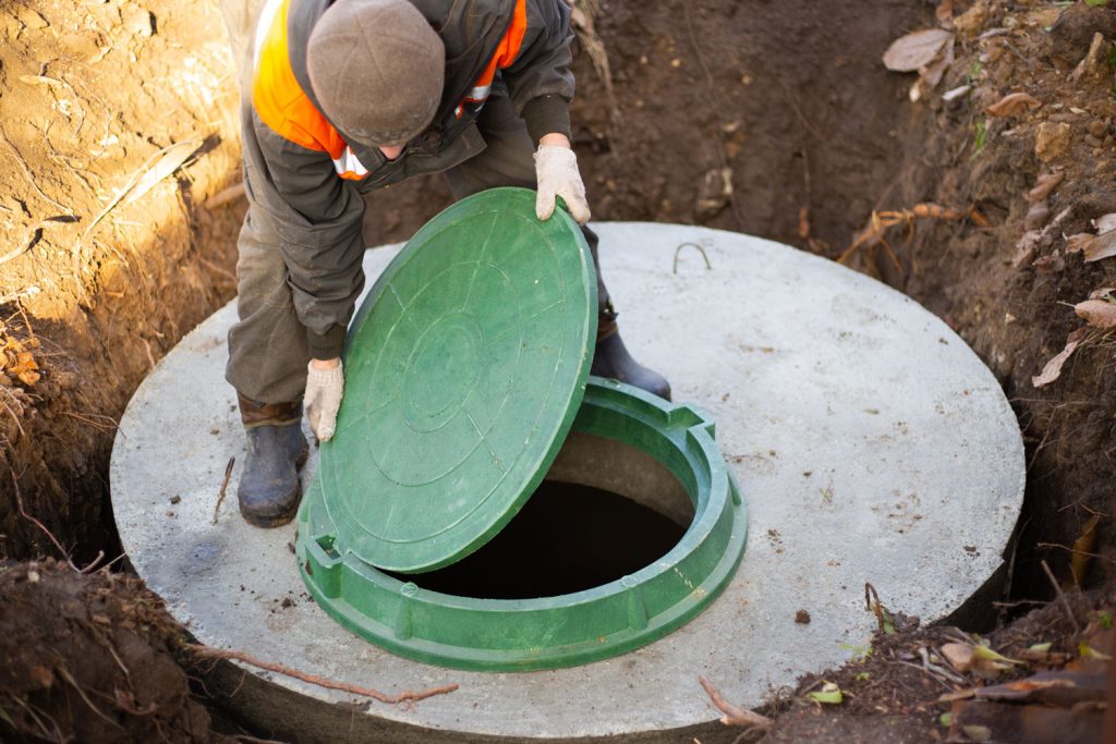 A worker installs a sewer manhole on a septic tank made of concrete rings.