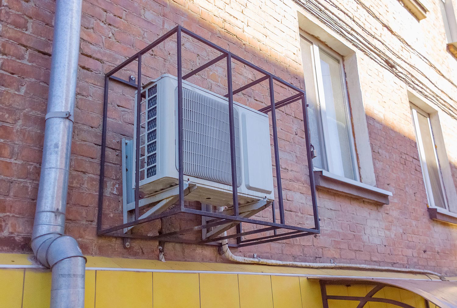 Air conditioning unit with anti-vandal metal grille on the brick wall
