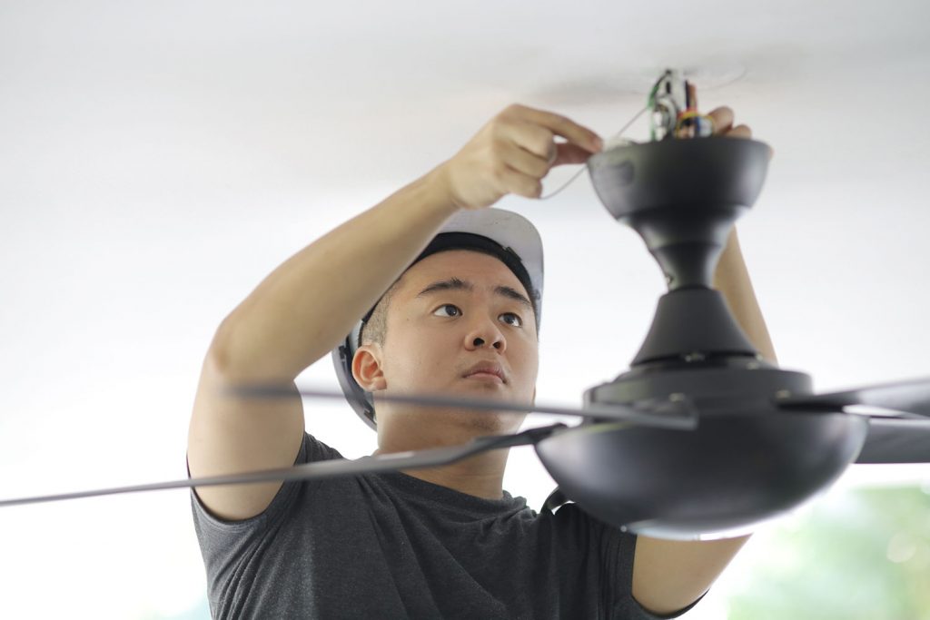 An Asian man is changing ceiling fan at residence.