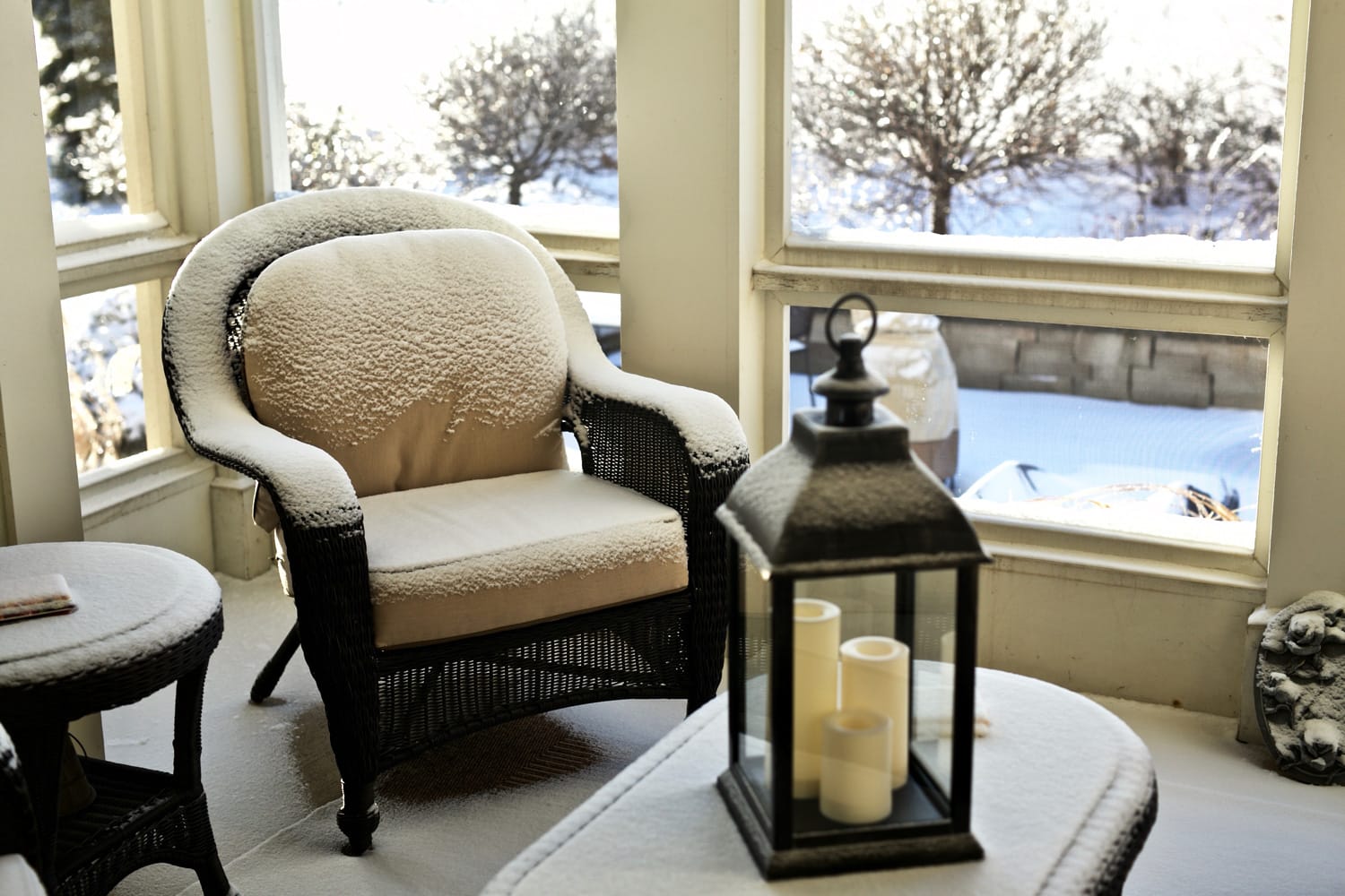Cozy, warm inviting scene on patio with snow covered furniture on screened porch with view of winter scene outside.