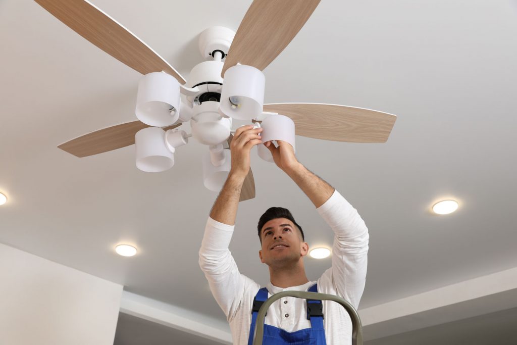 Electrician changing light bulb in ceiling fan indoors