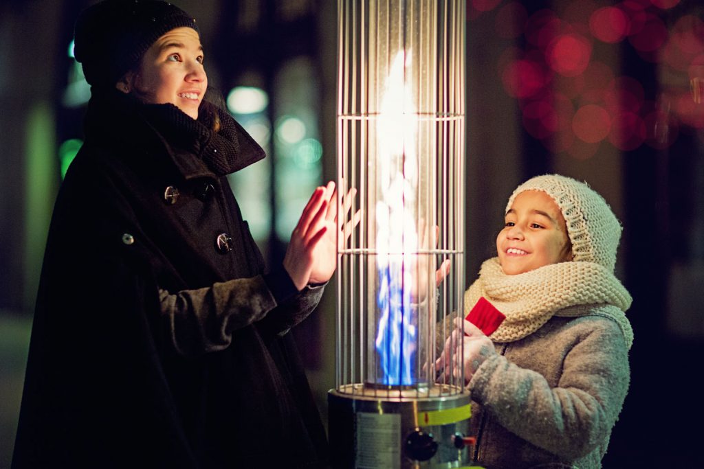 Girls are warming their hands on restaurant gas heater in the cold winter night