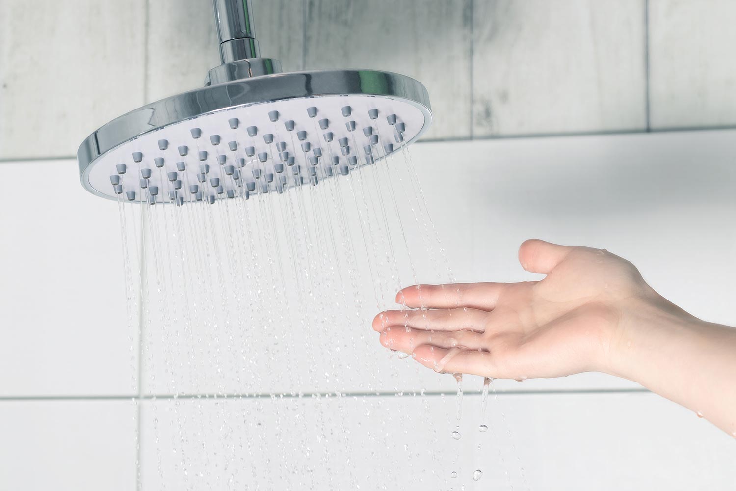 Hand touching water pouring from a rain shower head to check water temperature