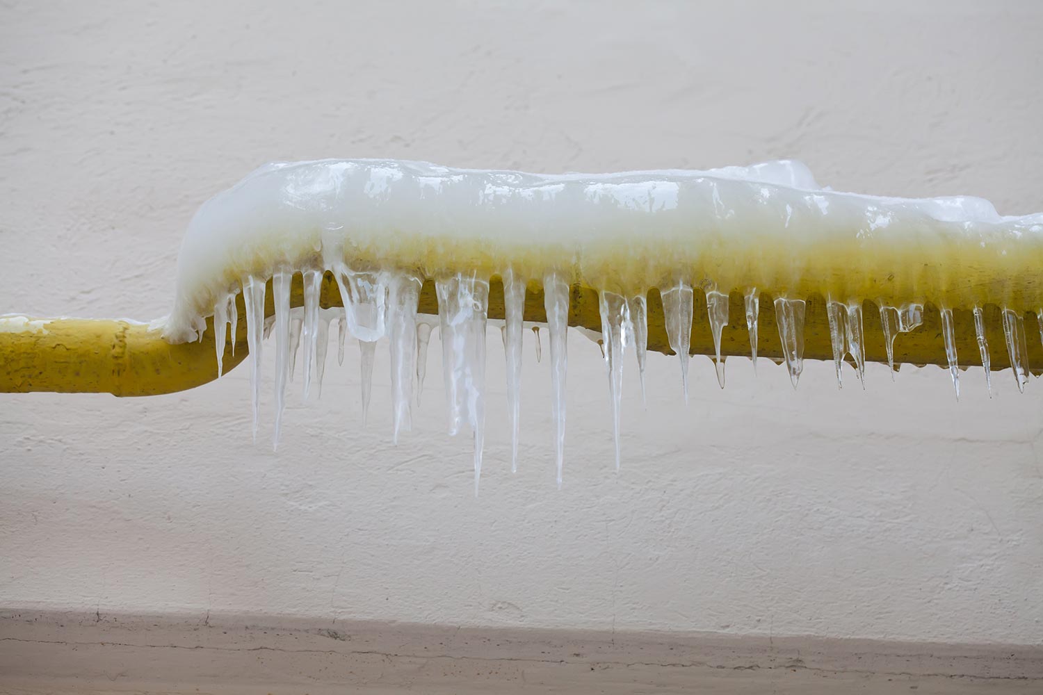 Icicles hanging from a frozen water yellow pipe
