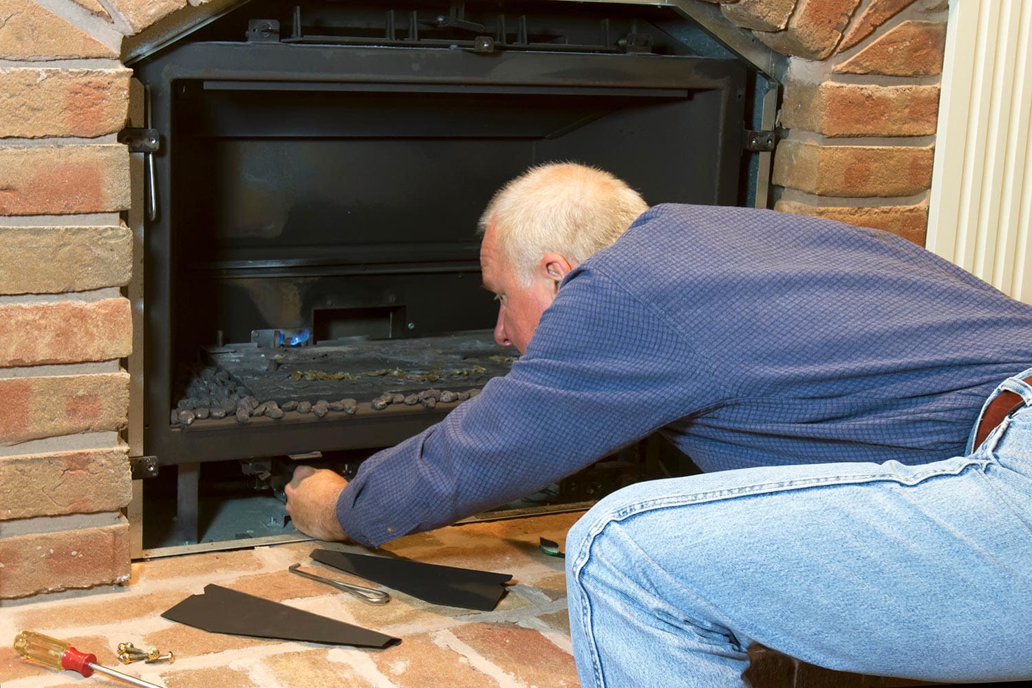 Man doing installation, repair, or seasonal maintenance on a built-in gas fireplace