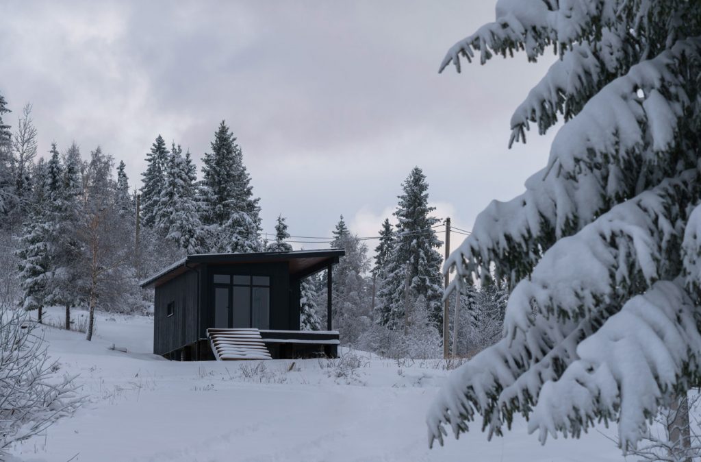 Modern black color cabin hidden in snowy pine forest
