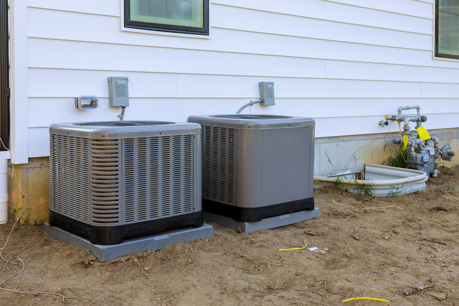 Small air conditioning units mounted on small concrete stands outside the house
