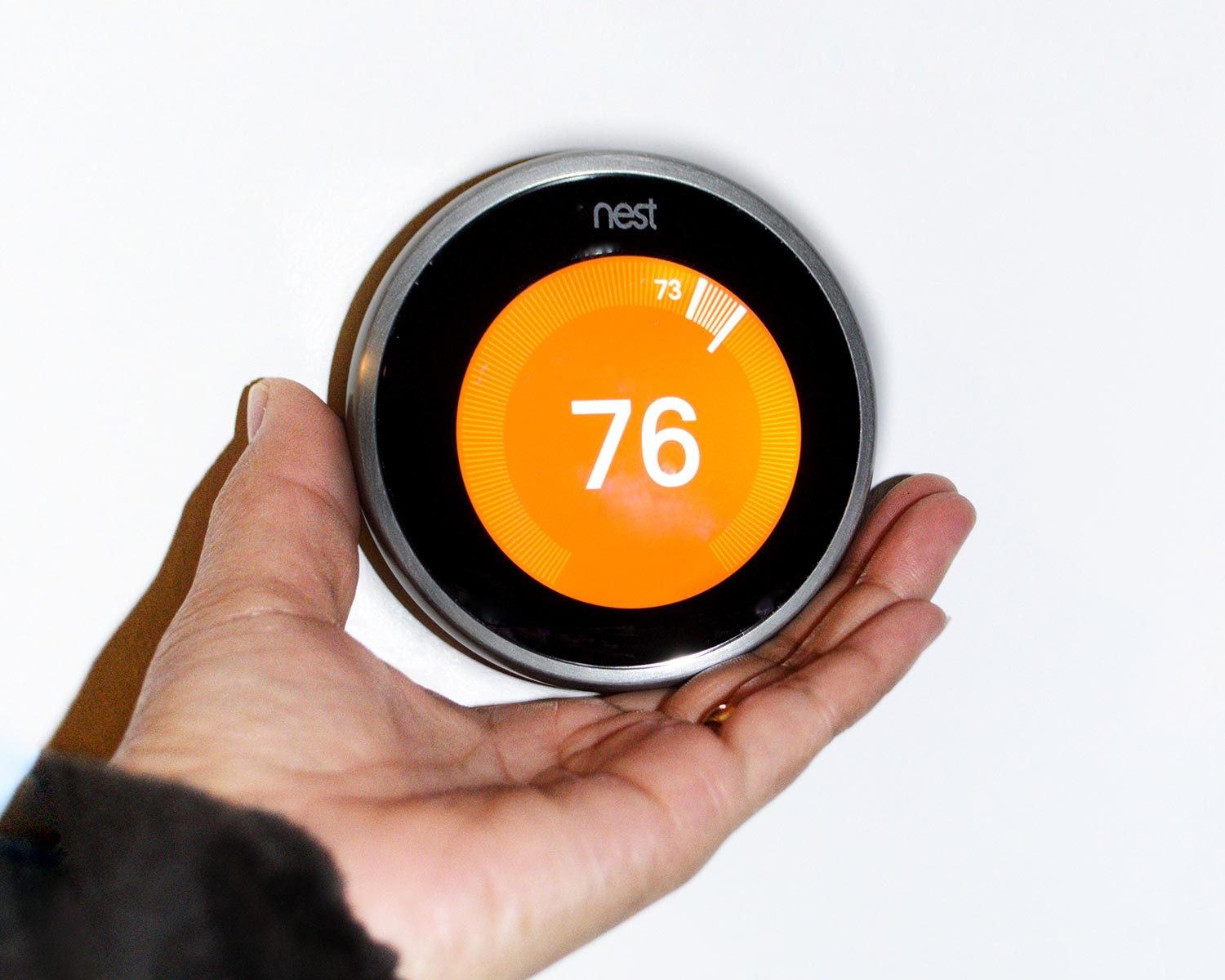 Women hand adjusting The Nest thermostats for. 73 to 76 Farenheit on heater
